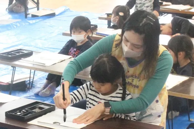 先生に筆の持ち方を教わる園児